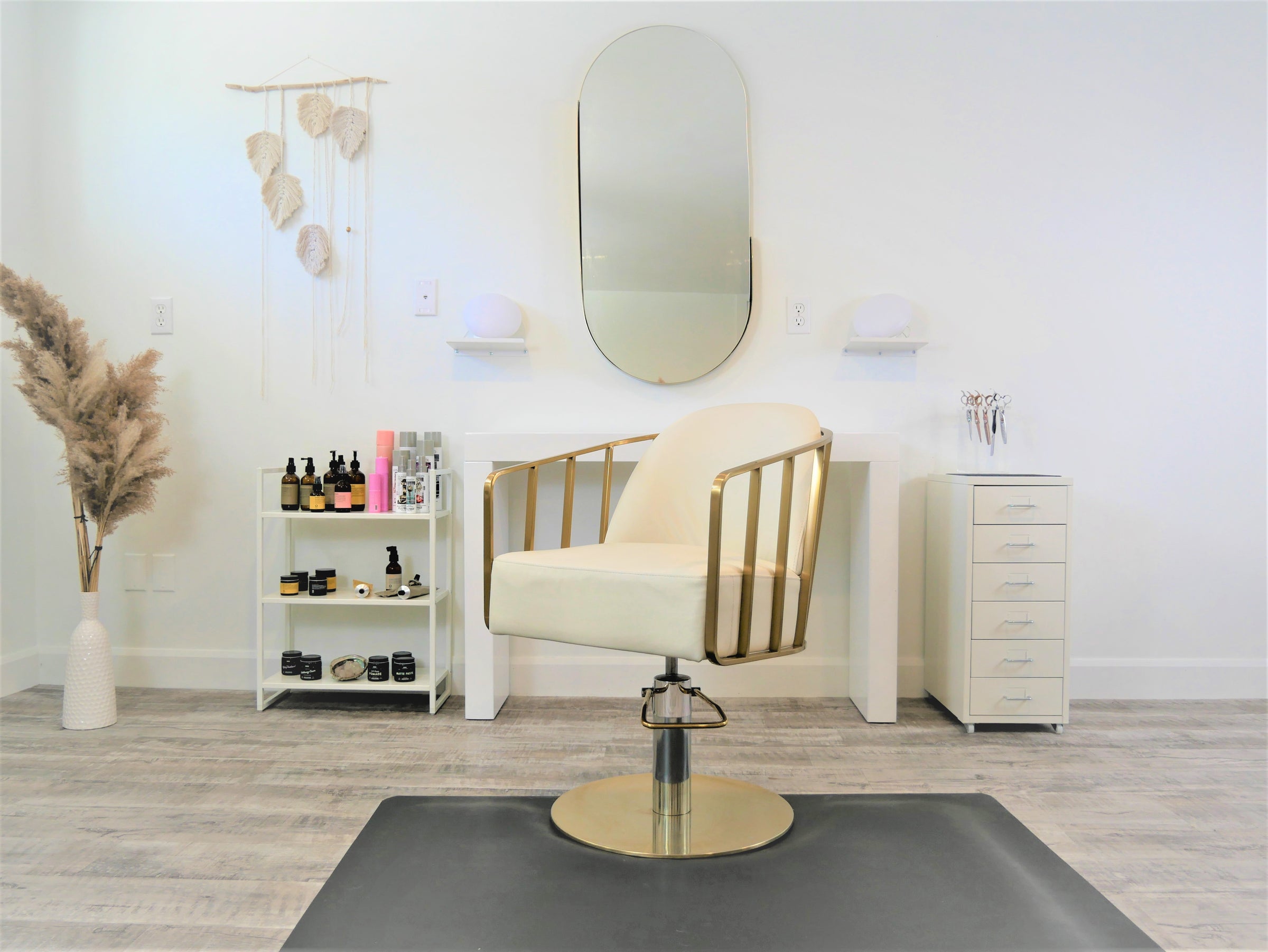 A photo of the main client seat in the studio; it shows a white spinning chair and behind it a desk and mirror, alongside are various high end beauty products and hair clippers.